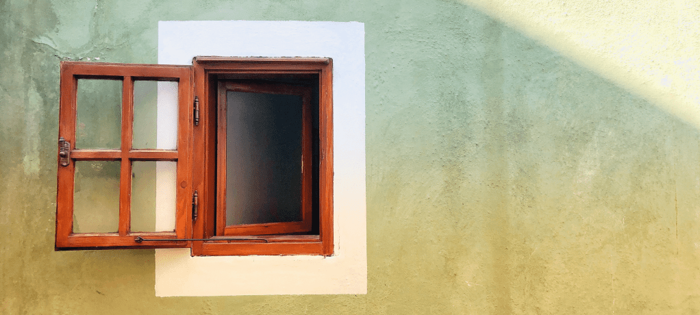 open stained wood frame window on mottled sunset shadowed cement wall