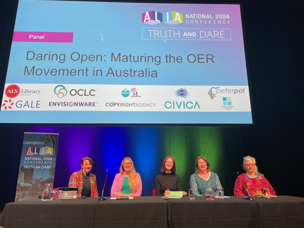ALIA National Panel smiling for the camera before the session begins: Katya Henry, Ash Barber, Sarah McQuillen, Angie Williamson, Jennifer Hurley. The title slide can be seen in the background: Daring Open: Maturing the OER Movement in Australasia